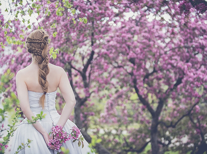 花が咲いている木の前でブーケを持っている女性の後ろ姿の画像